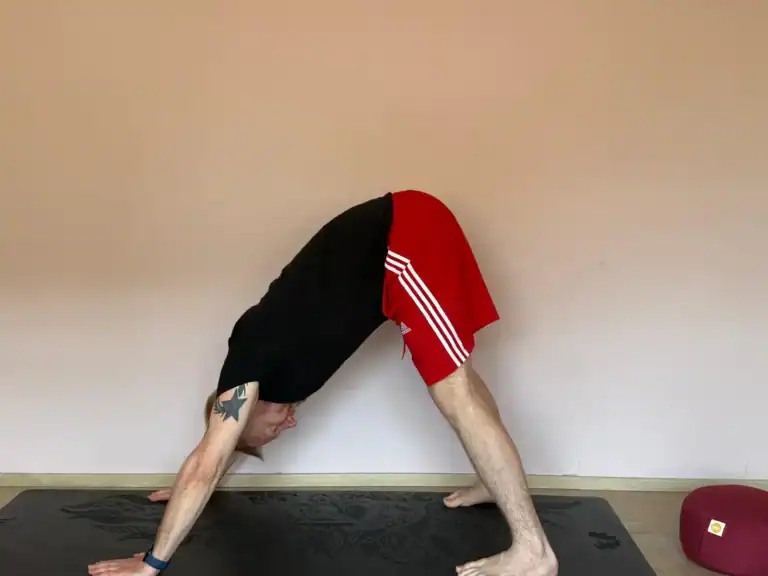 „Person übt die Yoga-Pose 'Herabschauender Hund' (Adho Mukha Svanasana) auf einer Yogamatte vor neutralem Hintergrund – ideal für Yoga Kurse online und das Üben zuhause.