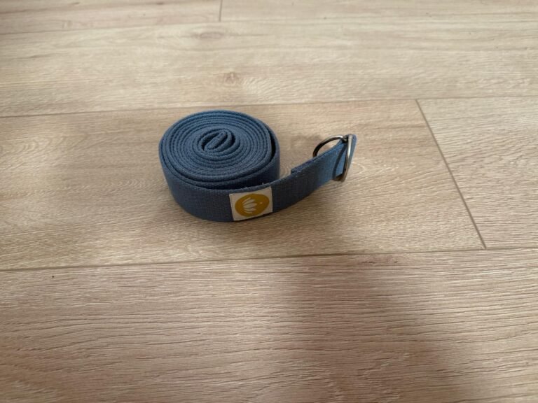 Gerollter Yogagurt aus robustem Stoff auf hellem Holzboden – hilfreiches Zubehör für Dehnungen und Haltungskorrekturen in deinen yoga kurse online.