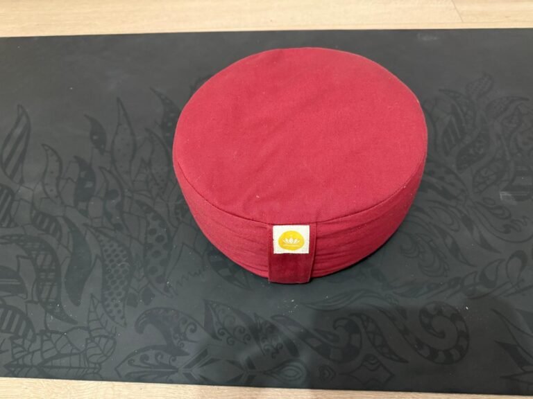 Rundes rotes Meditationskissen auf einer schwarzen Yogamatte – komfortable Sitzunterstützung für Meditation und Entspannung in deinen yoga kurse online.