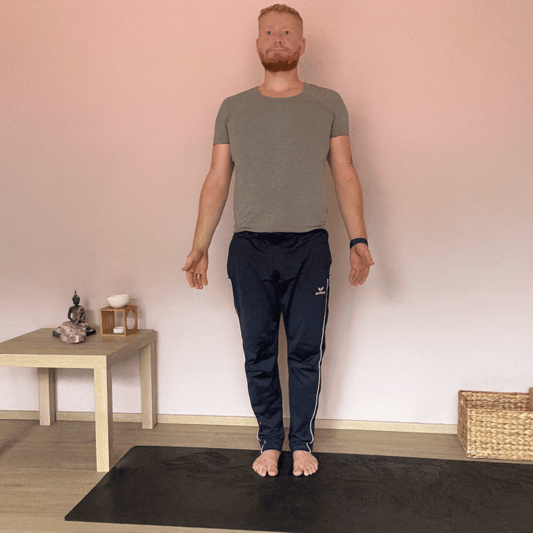 Mann übt Vrikshasana, die Baumhaltung im Yoga. Ein Fuß steht fest auf der Matte, der andere liegt am Oberschenkel, Hände über dem Kopf gefaltet. Diese Yoga Übung fördert Gleichgewicht, Konzentration und innere Ruhe.
