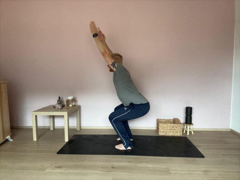 Mann praktiziert Yoga am Morgen in der Stuhlhaltung (Utkatasana) auf einer Matte, mit gestreckten Armen nach oben, zur Kräftigung von Beinen, Rücken und Schultern.