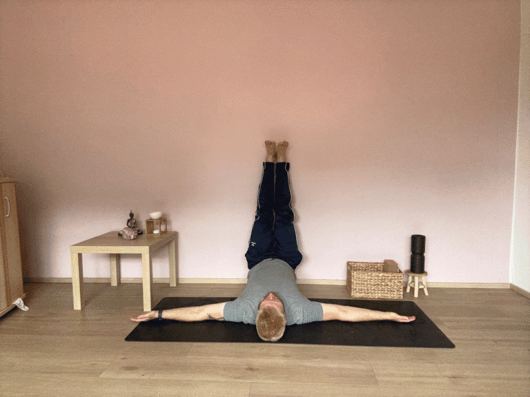 Mann übt Viparita Karani, die Umkehrhaltung „Beine an der Wand“ im Yoga. Der Oberkörper liegt entspannt am Boden, die Beine sind senkrecht an der Wand ausgestreckt, die Arme seitlich geöffnet. Diese sanfte Yoga Übung fördert Entspannung, verbessert die Durchblutung und beruhigt das Nervensystem.