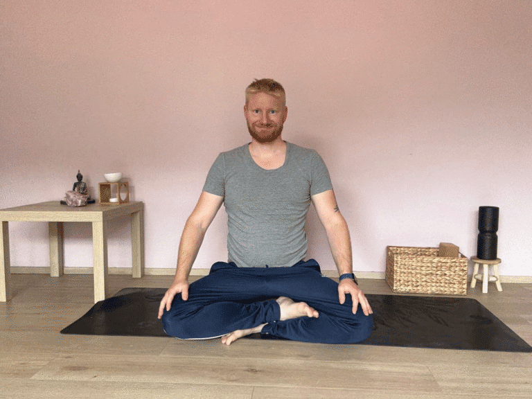„David Train sitzt im Schneidersitz auf einer Yogamatte in einem ruhigen Raum, bereit für eine Meditation oder Yoga-Praxis