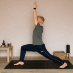 Mann führt die Yoga-Pose Krieger I (Virabhadrasana I) auf einer Yogamatte im Wohnzimmer aus – ein Beispiel für einfache Yoga Übungen für Anfänger zur Verbesserung von Balance, Kraft und Konzentration.