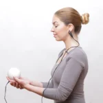 Frau misst mit dem Qiu Ball und Ohrclip ihr Stresslevel – HRV-Biofeedback zur Stress Messung und Entspannung.