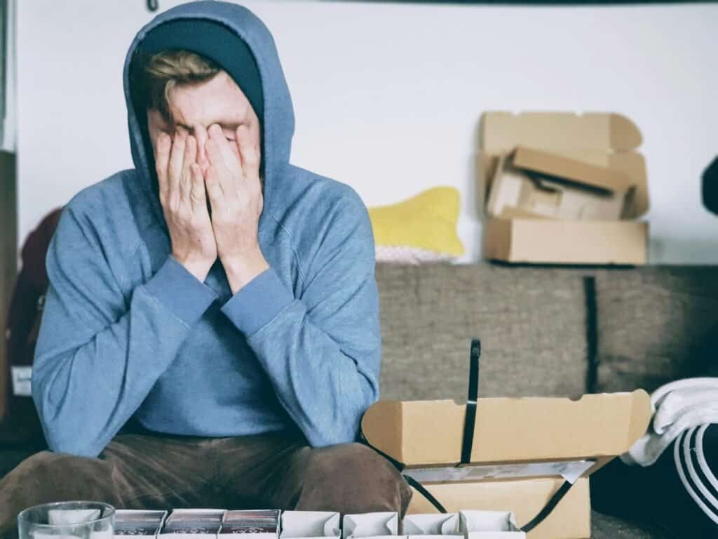 Mann sitzt mit Kapuzenpullover auf dem Sofa und hält verzweifelt den Kopf in den Händen. Symbolbild für Stress, Überforderung und psychische Belastung.