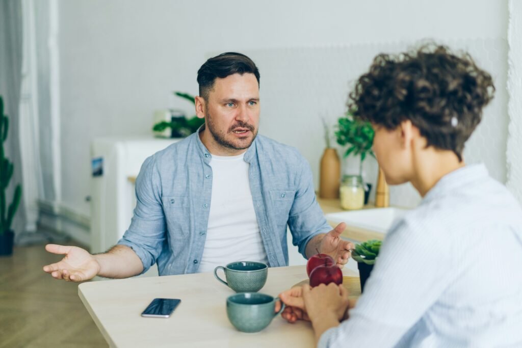 Zwei Menschen sitzen am Tisch und führen ein intensives Gespräch bei einer Tasse Tee – Symbol für zwischenmenschlichen Stress, Missverständnisse und emotionale Anspannung. Das Bild verdeutlicht, wie soziale Konflikte chronischen Stress verstärken können und warum es wichtig ist, den Vagus Nerv zu beruhigen, um innere Ruhe und Empathie wiederzufinden.