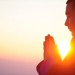 Person meditiert mit geschlossenen Augen im Sonnenaufgang – Symbol für inneren Frieden und bewusste Präsenz, wie sie in einem Kurs für Achtsamkeit oder einem MBSR Kurs online vermittelt wird.