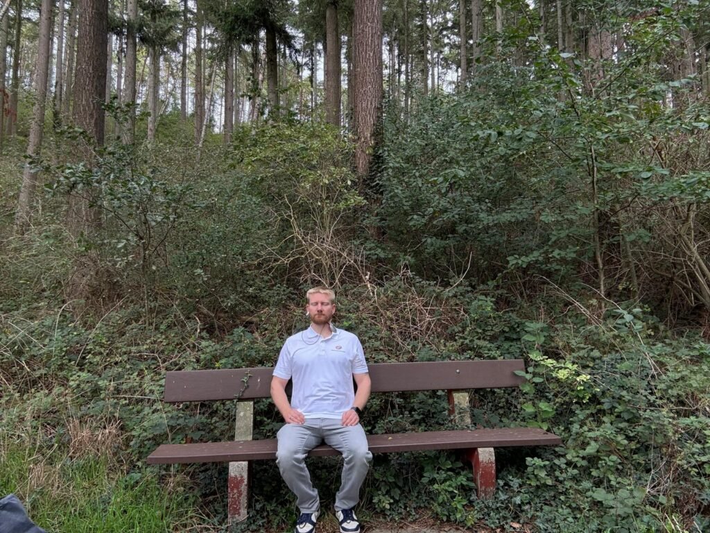 Mann sitzt meditierend auf einer Bank im Wald und nutzt den HeartMath Inner Balance Sensor für Herz-Kohärenz-Training.