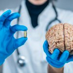 Arzt mit blauen Handschuhen hält ein menschliches Gehirn in der einen Hand und eine Kapsel in der anderen – Symbolbild für den Placebo Effekt, die Wirkung von Glauben und Erwartung auf das Gehirn und die Gesundheit.