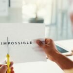 Person schneidet das Wort „impossible“ auf einem Blatt Papier auseinander – Symbol für positive Glaubenssätze, innere Blockaden auflösen, Unterbewusstsein neu programmieren und die Kraft der Gedanken bewusst nutzen.