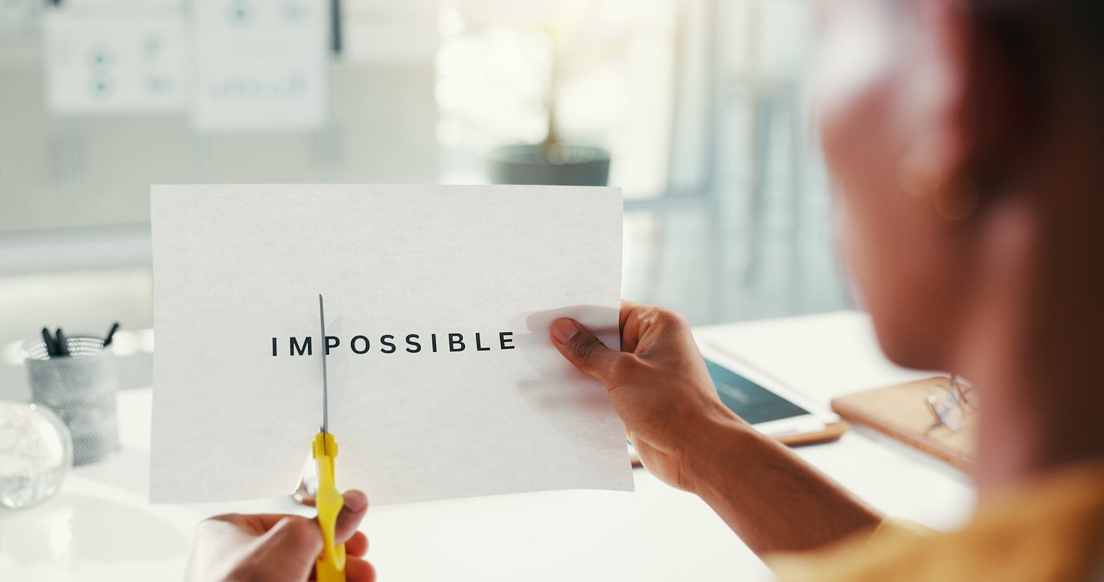 Person schneidet das Wort „impossible“ auf einem Blatt Papier auseinander – Symbol für positive Glaubenssätze, innere Blockaden auflösen, Unterbewusstsein neu programmieren und die Kraft der Gedanken bewusst nutzen.