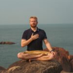 Mann meditiert am Meer und praktiziert kohärente Atmung zur Förderung von Herzkohärenz und innerer Ruhe während einer Herzkohärenz Meditation.