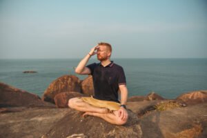 Person praktiziert Atemübungen zur Entspannung am Meer und macht in meditativer Sitzhaltung Atemübungen gegen Stress und Angst.