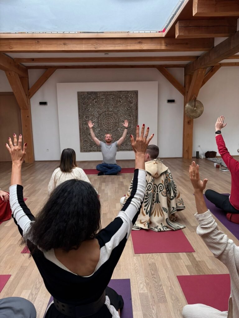 Breathwork Coach David Train leitet eine Transformative Breathwork Gruppensession – Teilnehmende stehen auf Yogamatten mit ausgestreckten Armen in einem hellen, stimmungsvollen Raum mit Holzbalken und warmer Atmosphäre.