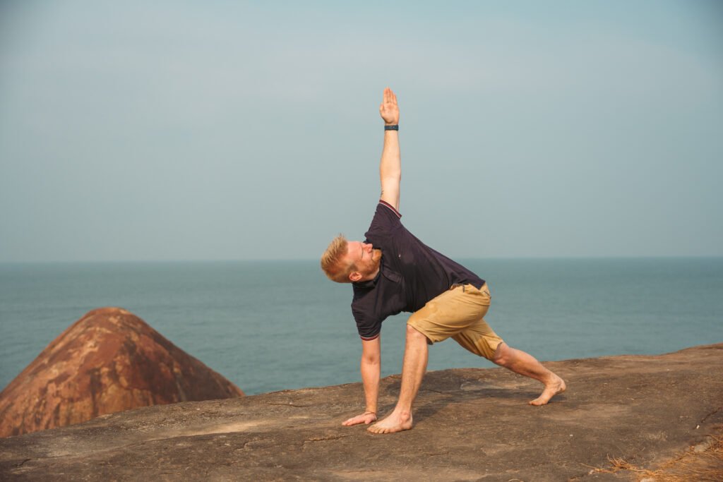 Mann übt eine stehende Yoga-Pose auf Felsen am Meer – Yoga für Anfänger im Freien