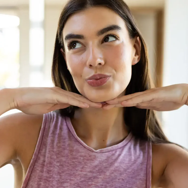 Frau führt eine Gesichtsübung durch und legt die Hände unter das Kinn – ideal als Teil eines Face Yoga Online Kurses, um Gesichtsmuskeln zu aktivieren und zu straffen.